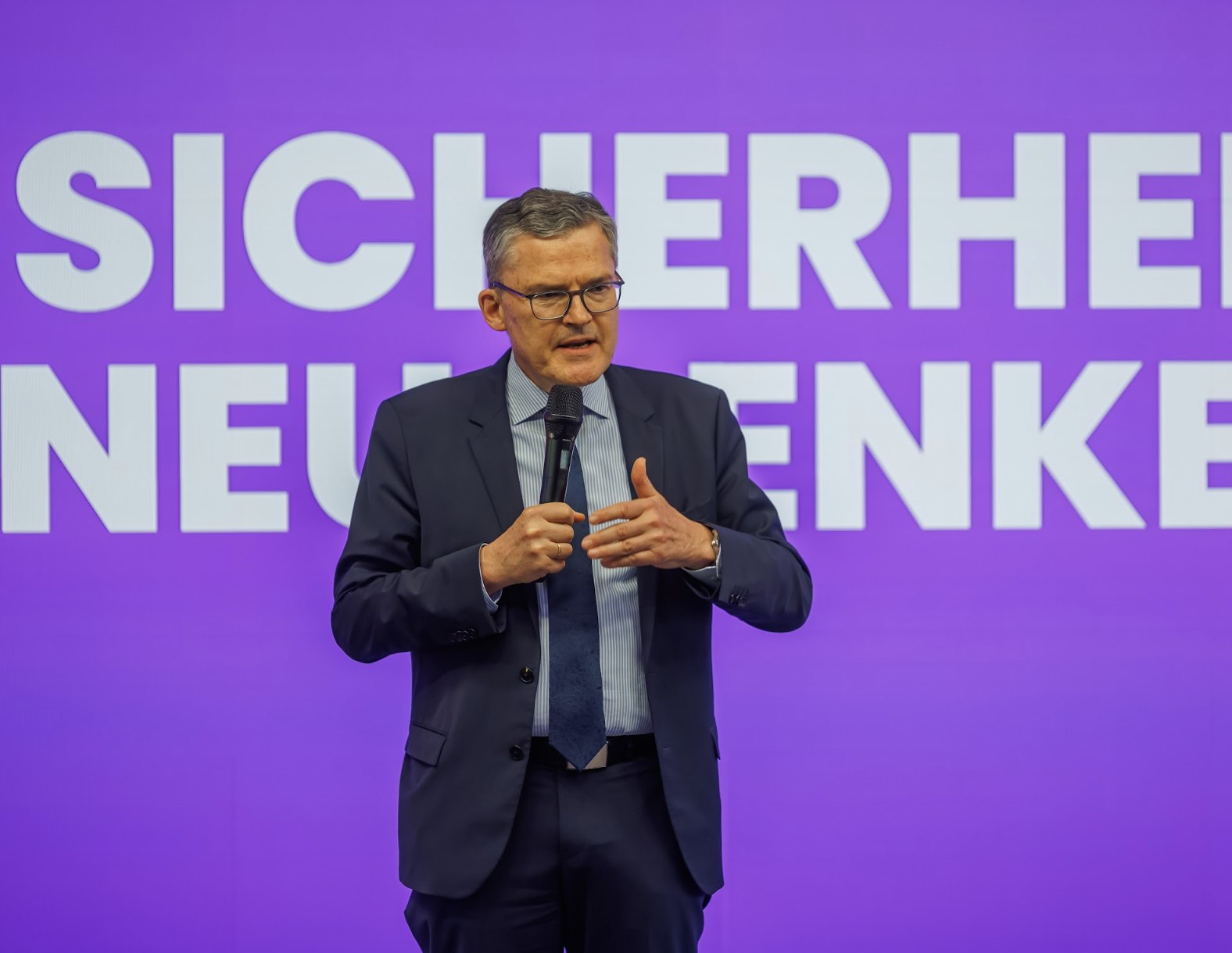 Neu Denken – Redner auf der Bühne vor Konferenz-Backdrop